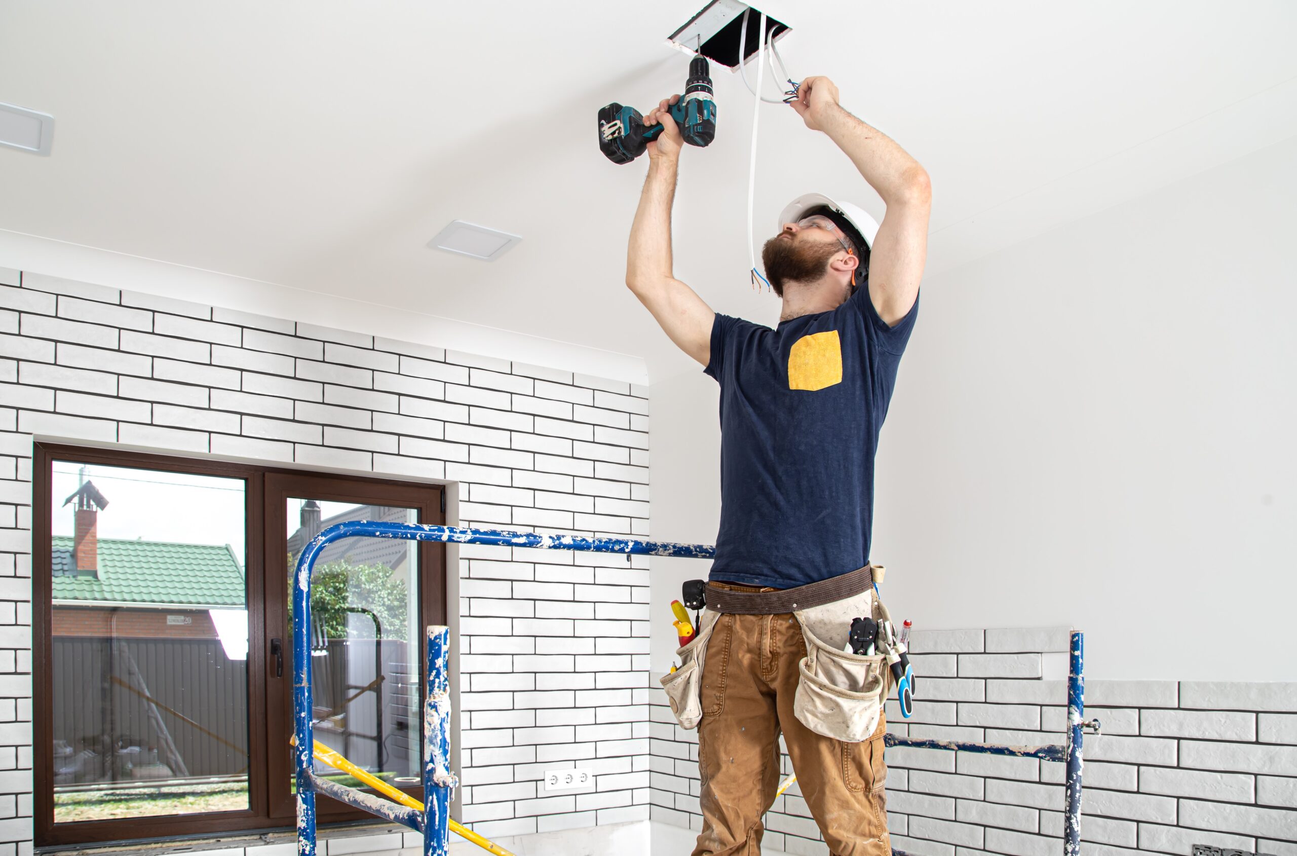 Home electrician builder work installation lamps height professional overalls with drill repair site